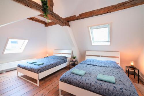 two beds in a bedroom with wooden floors and two windows at Antwerp Old Town Centrum Apartment in Antwerp