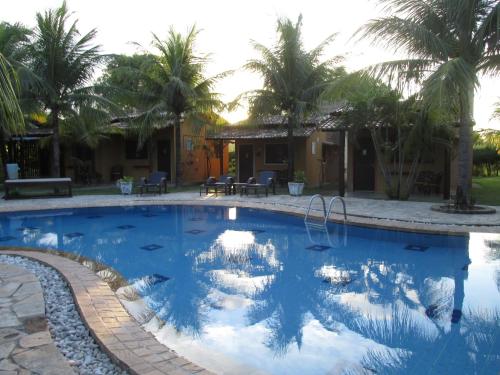 a pool with palm trees and a house in the background at Hotel Enseada Maracajaú in Maracajaú