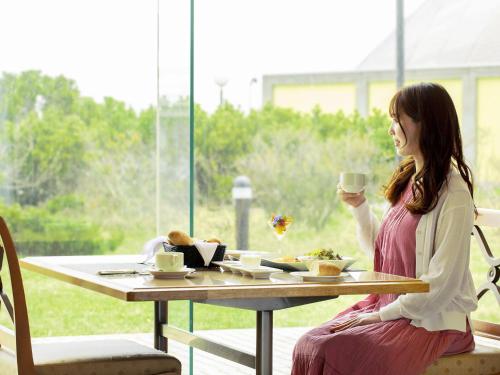 a woman sitting at a table with a cup of coffee at Surfeel Hotel Wakkanai in Wakkanai