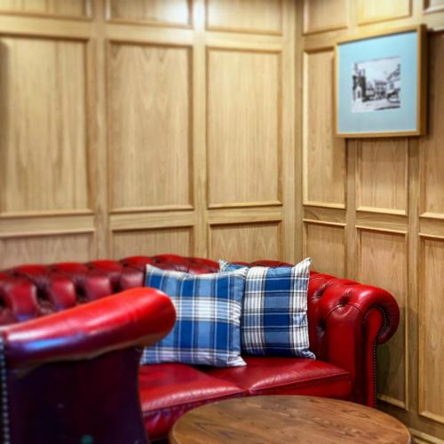 a red leather couch with two pillows and a table at Kings Arms Hotel in Lockerbie