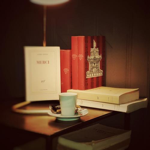 a table with books and a coffee cup and a laptop at L'Instant Sévigné in Grignan