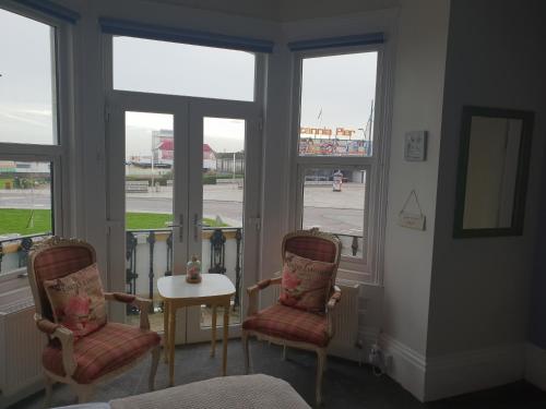 um quarto com duas cadeiras, uma mesa e janelas em Henrys on the Prom em Great Yarmouth