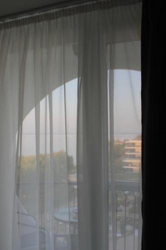 a window with white curtains and a table with chairs at Vízparti Apartman in Siófok