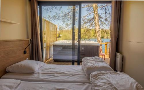 a bedroom with a bed and a balcony with a tub at Camping du Château Vert in Hondainville