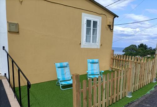 two blue chairs sitting outside of a house with a fence at O Chaleco in San Ciprián