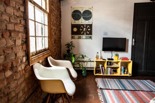 a living room with two white chairs and a tv at NeighborHUB hostel e coliving in Sao Paulo