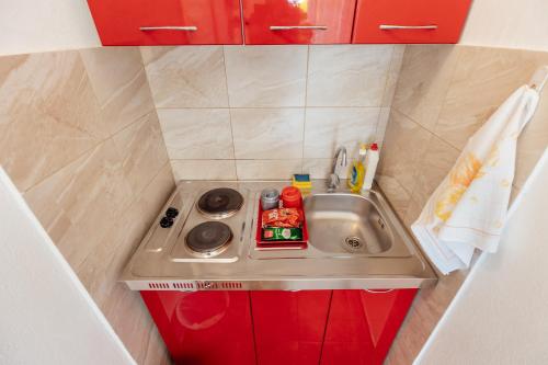 uma pequena cozinha com um lavatório e armários vermelhos em Anastasija5 em Herceg-Novi