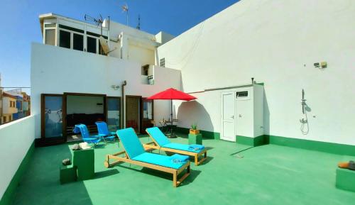 a patio with blue chairs and a red umbrella at Casa SOLEADA SUNNY House in Playa del Burrero