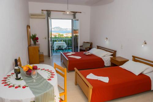 a room with two beds and a table and a balcony at Cleopatra Apartments in Laganas