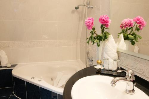 La salle de bains est pourvue d'un lavabo et d'une baignoire ornée de fleurs roses. dans l'établissement Schlosshotel zum Markgrafen, à Quedlinbourg