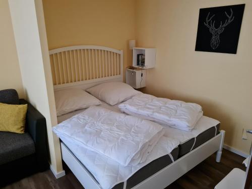 a bedroom with a bed with white sheets and a chair at Bergstation Altenau in Altenau