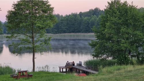 a person sitting on a dock on a lake at Domwigierski pl -Jeziorki -GR- Comfort-Ferienhaus-Polen - własna linia brzegowa i sauna in Wysoki Most