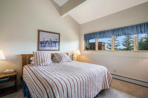 a bedroom with a bed with a striped comforter and two windows at Moraine 27 Townhouse near Gondola in Steamboat Springs