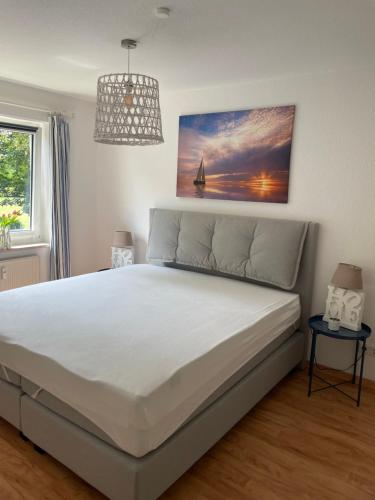 ein Schlafzimmer mit einem großen weißen Bett mit einem Gemälde an der Wand in der Unterkunft Fehmarn Oase in Petersdorf auf Fehmarn