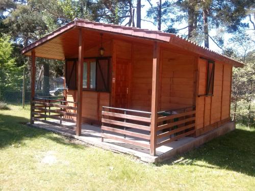 a wooden cabin with a porch in the grass at Camping Cobijo in Vinuesa