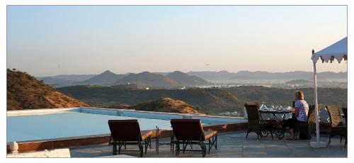 a woman sitting at a table next to a swimming pool at Fateh Garh Resort by Fateh Collection in Udaipur