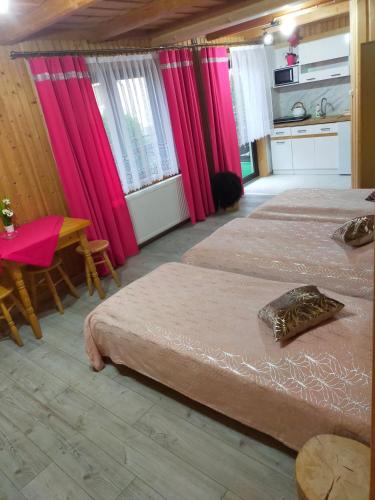 two beds in a room with pink curtains and a table at Sichlański Zakątek in Murzasichle