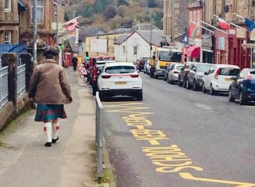 a woman walking down a city street with a car parked at The Sleeping Lion - Dunoon Holiday Home in Dunoon