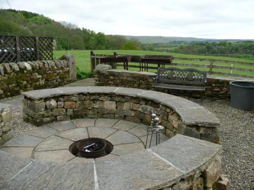 a stone fire pit in a yard with two benches at Hollybush Inn in Greenhaugh