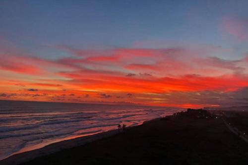 a sunset over the ocean with people standing on a beach at Relax en la playa con mas de 70 servicios in Progreso