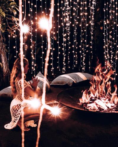 a woman in a dress sitting in front of a fire at Igloo Beach Lodge in Manuel Antonio