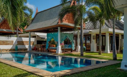 a swimming pool in front of a house with palm trees at Miskawaan Beachfront Villas in Mae Nam