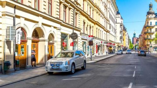 a white car driving down a city street with buildings at Nomad Cave in Stockholm