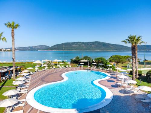 una piscina con ombrelloni e sedie e l'oceano di Hotel Corte Rosada Affiliated by Melia a Porto Conte