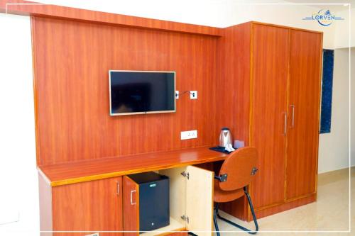 Habitación con pared de madera, TV y silla. en Hotel Lorven en Tirupati