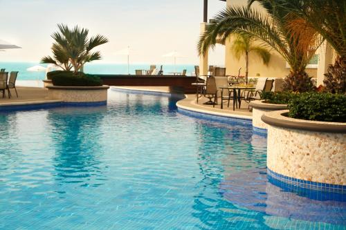a swimming pool with palm trees and a table and chairs at Diamond Bay in Mazatlán