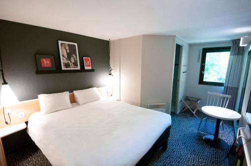 a hotel room with a large white bed and a table at ibis Maisons Laffitte in Maisons-Laffitte