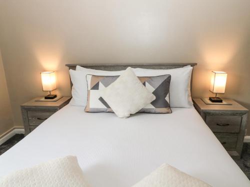 a bedroom with a white bed with two lamps at Asta Cottage in Morpeth
