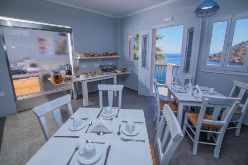 a dining room with white tables and chairs and the ocean at Niriides Hotel Apartments in Symi