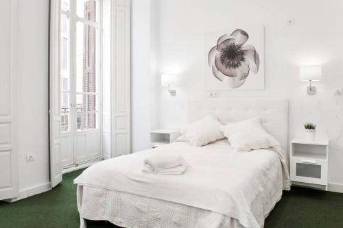 Un dormitorio blanco con una cama blanca con una flor en la pared en Company 34, en Málaga