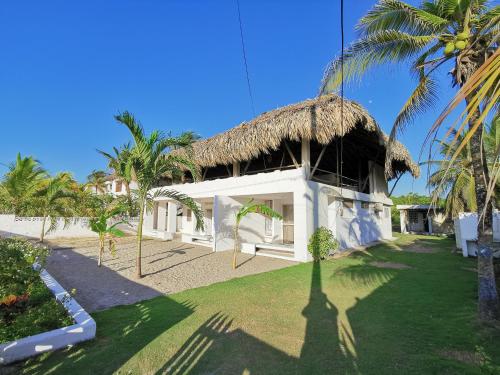 a building with a thatched roof and a yard with palm trees at Casa el Muelle in Coveñas