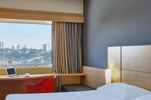 a hotel room with a bed and a desk and a window at ibis Sao Jose dos Campos Dutra in São José dos Campos