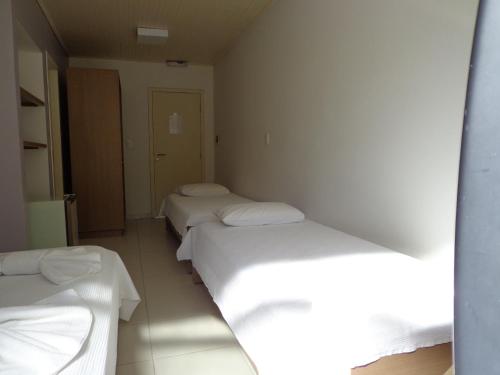 drie bedden in een kamer met witte lakens bij Hotel Abrolhos in Nova Viçosa