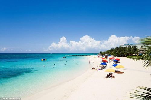 a beach with umbrellas and people in the water at J Ochi ApartHotel in Ocho Rios