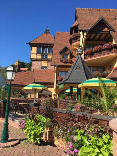 a building with tables and umbrellas in front of it at Hotel Le Mandelberg in Mittelwihr