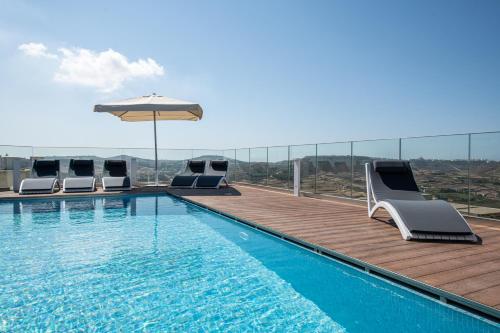 a swimming pool with chairs and an umbrella on a building at Bliss Boutique Living in Xagħra