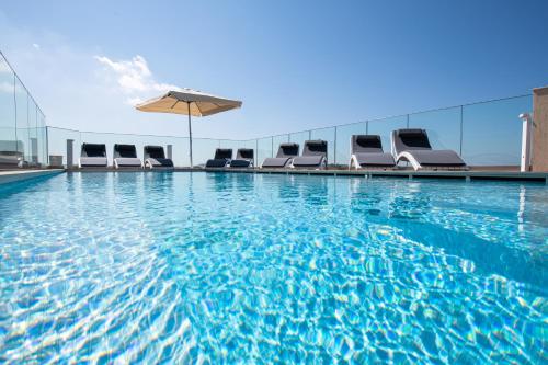 a swimming pool with chairs and an umbrella at Bliss Boutique Living in Xagħra