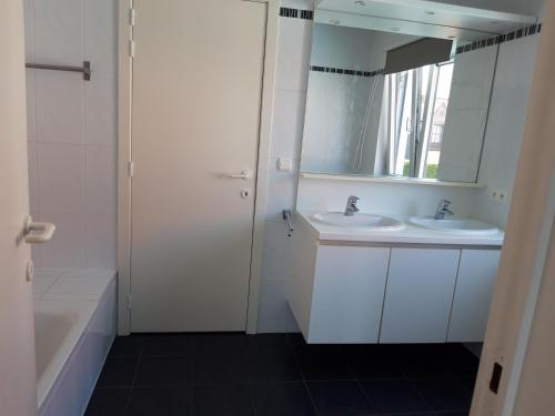 a white bathroom with two sinks and a mirror at Duplex met zwembad Neoportus in Nieuwpoort