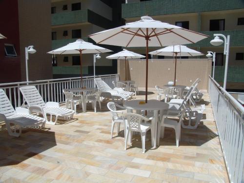un patio con tavoli e sedie bianchi e ombrelloni di Condomínio Pedra Coral a Ubatuba