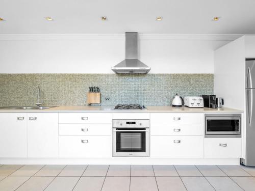a kitchen with white cabinets and a stove top oven at Neptune Hyams Beach in Hyams Beach