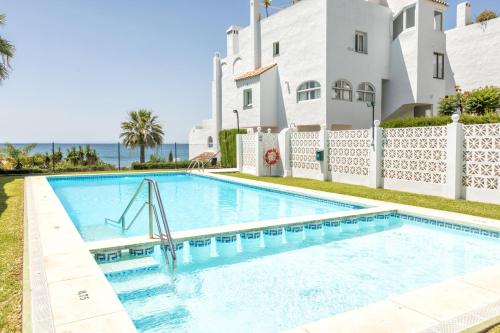 a swimming pool in front of a house with the ocean at Front Sea View Penthouse in Estepona