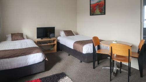 a room with two beds and a table and a tv at Fiesta Court Motel in Whanganui