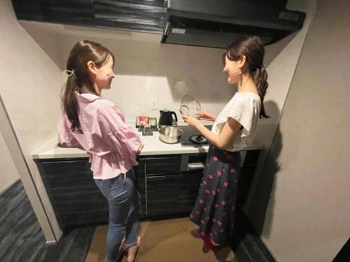 two girls standing in a kitchen preparing food at RESI STAY Mayu Grace Hotel in Kyoto