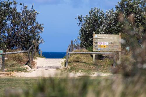a wooden sign on a dirt road with trees and acknowled at Sails Luxury Apartments Merimbula in Merimbula