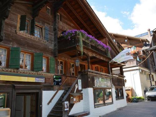 a wooden building with a balcony with purple flowers on it at Apartment Le Vieux Chalet by Interhome in Gstaad