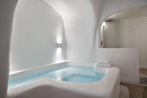 a bath tub in a bathroom with a mirror at Katikies Kirini Santorini - The Leading Hotels Of The World in Oia